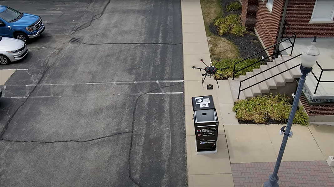 Photo of aerial drone delivering a small package into a custom built mailbox by lowering the item in with a cable.